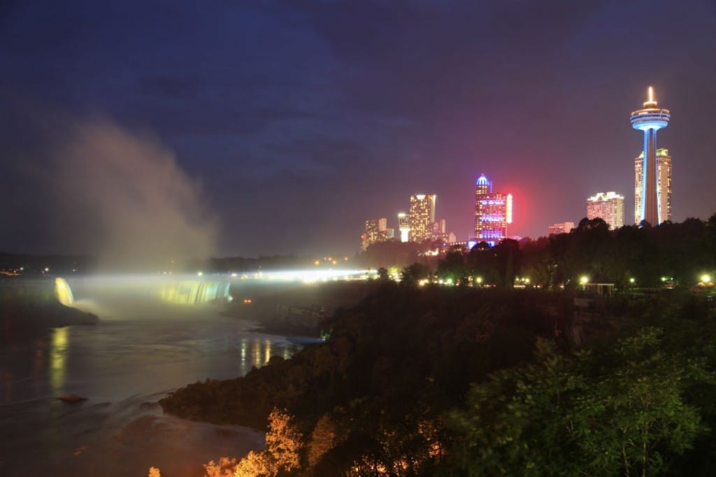 Niagara falls water grass trees and surrounding buildings that are lighted up at night